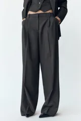 Pantalón gris de tiro alto con pinzas delanteras, bolsillos frontales y pernera ancha. Cierre frontal con cremallera, botón interior y gancho.