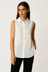 Camisa blanca de algodón con broderie, sin mangas, con cuello camisero y cierre frontal con botones.