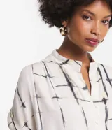 Vestido midi de viscosa color blanco con estampado de bloques negros, corte evasé, mangas cortas, cuello camisero, lazo en la cintura y cierre frontal con botones.