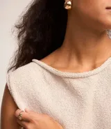 Blusa de punto color beige, sin mangas, con escote redondo y bajo asimétrico.