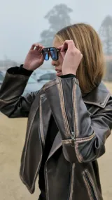 Chaqueta de cuero ovino color marrón, con cuello clásico, cierre asimétrico con cremallera, solapas con botones a presión, múltiples bolsillos con cremallera y cinturón ajustable en la cintura.
