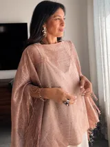 Poncho tejido color rosa con detalles brillantes y flecos en el ruedo.