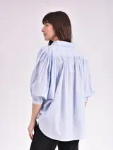 Camisa celeste con cuello mao, corte holgado, mangas 3/4 abullonadas con puños elásticos y cierre frontal con botones.