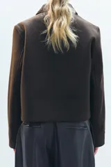 Chaqueta corta negra de cuello solapa y manga larga con puños. Tiene bolsillos de parche en el frente y cierre frontal con botones.