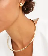 Conjunto de caravana y collar corto femenino en metal dorado. La caravana es pequeña, redonda y metálica con cierre a tornillo. El collar es corto, con forma tubular y cierre por enganche.