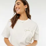 Camiseta blanca de algodón con cuello redondo y mangas cortas. Presenta un bolsillo en el pecho con dos lazos decorativos.