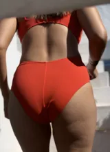 Traje de baño enterizo color naranja con breteles finos y abertura en la zona del abdomen.