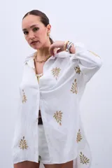 Camisa blanca de manga larga con bordado de hojas doradas.
