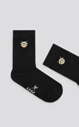 Medias negras de caña media con diseño de vaca bordado en la parte superior y logo de la marca con tijeras en la planta del pie.