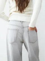 Jean de tiro alto color gris claro, corte loose con pernera ancha. Diseño clásico de cinco bolsillos con cierre de cremallera y botón metálico.