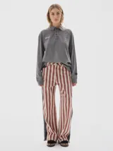 Pantalón de jean de tiro alto, pierna ancha y recta, con estampado de rayas verticales en tonos rojo óxido y beige claro. Presenta un panel lateral oscuro con textura de estampado sutil.