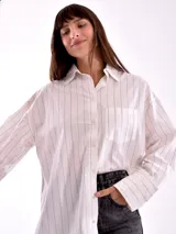 Camisa blanca con rayas verticales negras, de corte holgado, manga larga con puños abotonados y bolsillo en el pecho.