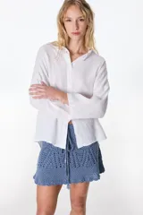 Camisa de lino color blanco, de manga larga y corte holgado, con cuello camisero y cierre frontal de botones.