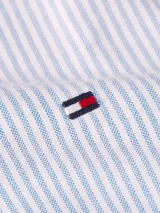 Camisa de manga corta Tommy Hilfiger Heritage, de corte regular, confeccionada en tela Oxford a rayas verticales celestes y blancas. Tiene cuello abotonado, cierre con botones y logo de Tommy Hilfiger bordado en el pecho.