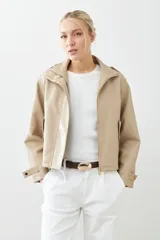 Chaqueta corta color beige de cuero sintético, con cuello alto, cierre frontal con botones a presión y bolsillos laterales con solapa.