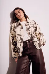 Campera de algodón color crema con estampado de manchas marrones tipo vaca, corte al cuerpo, con cuello clásico, cierre frontal con botones y bolsillos de parche en el pecho.