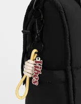 Cartera shopper negra de tela deportiva con doble asa corta estampada, correa regulable y desmontable, cierre superior con puller de goma y charm lateral.