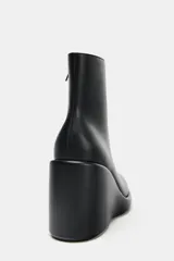 Botín negro de cuero sintético con cuña alta y punta redonda. Cierre con cremallera lateral.