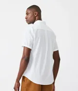 Camisa de hombre de manga corta en lino color blanco, con cuello clásico, botonadura frontal y bolsillo de parche en el pecho. Corte recto.