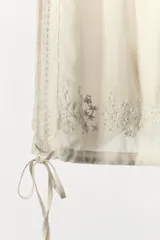 Shorts de tiro alto color crudo, con cintura elástica ajustable con lazada. Detalle de bordados florales combinados a tono, aplicación de puntilla y abalorios. Bajo acabado con tira ajustable.