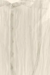 Camisa color crudo de corte holgado, confeccionada en hilatura con lino y tejido con efecto arrugado. Tiene cuello solapa, mangas largas con puños, bajo asimétrico con aberturas laterales y cierre frontal con botones.