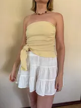 Top strapless asimétrico color amarillo manteca, con detalle de nudo lateral y textura arrugada.