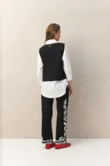 Chaleco blanco de algodón con bordados de cadenas doradas y lazos frontales.