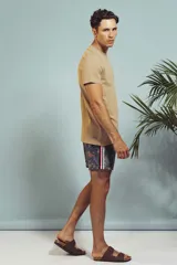 Short de baño con estampado de hojas en tonos grises y celestes, con cordón ajustable en la cintura y detalle de franja lateral con rayas rojas, blancas y negras.