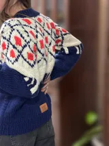 Sweater de lana merino con cuello redondo y diseño con motivos geométricos en tonos azul, marrón, naranja, verde y beige.
