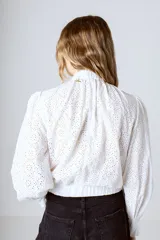 Blusa blanca de broderie con cuello alto, mangas largas abullonadas y puños elásticos.
