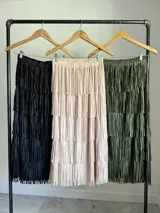 Maxi falda con múltiples capas de flecos, confeccionada en tela elastizada. Disponible en negro, beige y verde militar.