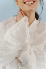 Blusa color rosa pálido de tejido fresco y liviano, con cuello alto con lazo y mangas largas con volados.