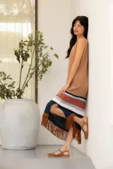 Vestido tejido en hilado de algodón con flecos de gamuza color tostado, con rayas horizontales en el ruedo en tonos negro, blanco, ladrillo y celeste.