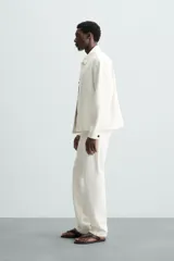 Pantalón de jean color blanco, corte recto, con bolsillos frontales y traseros, y cierre frontal con cremallera y botón.