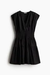 Vestido corto negro sin mangas en tejido fresco de algodón. Modelo con escote cruzado en V, pliegues en los hombros, cintura fruncida y pollera con vuelo.
