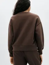 Buzo de tejido de punto color gris melange, con cuello redondo y corte holgado. Presenta costuras visibles en los hombros y puños y cintura acanalados.