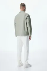 Sobrecamisa verde oliva de corte recto, con cuello inglés, cierre frontal con botones a presión y dos bolsillos de parche con solapa en el pecho.