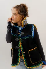 Chaleco negro de corderito con cierre de alamares y tejido a mano en crochet con detalles en amarillo, verde, celeste y azul.