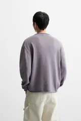 Jersey de hombre color lila, tejido en hilatura de algodón con textura. Tiene cuello redondo, manga larga y acabados en rib con detalle de vuelta.