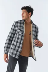 Sobrecamisa de algodón para hombre con interior de corderito, estampado a cuadros en tonos negro, blanco y azul. Tiene cierre de botones, bolsillos tipo cartera y logo en goma. El modelo usa talle M.