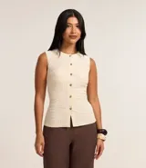 Blusa femenina de corte regular confeccionada en tejido de anarruga texturizado color beige. Presenta cuello redondo, diseño sin mangas y cierre frontal con botones.