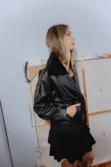 Campera bomber negra de cuero con cuello de piel sintética, forro interior y detalles de pasamanería en cuero marrón gastado.