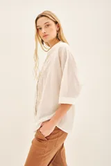 Camisa blanca de voile con rayas finas, corte amplio, cartera con botones y bordado de flores en el frente.