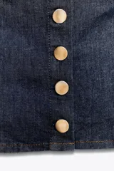 Top corto de denim azul oscuro, con escote en pico, tirantes anchos y cierre frontal con botones metálicos dorados.