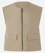 Chaleco color beige de corte sastrero con cierre frontal de cremallera, cuello redondo y bolsillos con solapa.