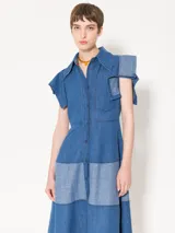 Vestido camisero midi de denim azul con silueta relajada. Tiene mangas cortas rebatidas, recorte a contratono en la falda y acceso frontal con botones.