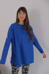Buzo azul de viscosa con cuello redondo y manga larga. Presenta un aplique con diseño geométrico en el brazo izquierdo.