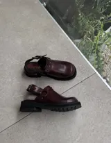 Zueco de cuero vacuno color bordó, con forrería vacuna, detalle de herrajes oro viejo y estribo. Tiene un taco de 4,5 cm y suela de goma.