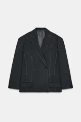 Blazer negro oversize de cuello solapa y manga larga con hombreras. Bolsillos con solapa en delantero y de vivo en pecho. Detalle de pespuntes combinados a contraste. Forro interior. Cierre frontal cruzado con botones.