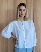 Camisa blanca con bordado floral, cuello redondo y mangas 3/4 abullonadas con puños elásticos. Cierre frontal con botones.